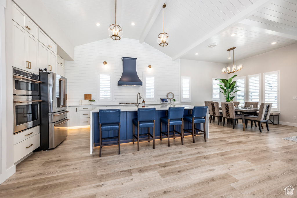 Kitchen featuring pendant lighting, appliances with stainless steel finishes, white cabinets, a center island with sink, and light wood-type flooring