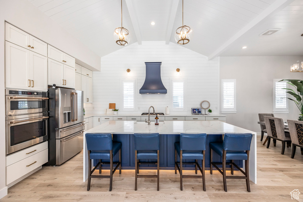 Kitchen with white cabinetry, a center island with sink, light wood-type flooring, custom range hood, and stainless steel appliances
