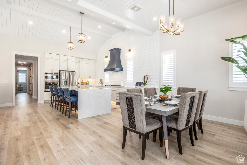 Dining area with an inviting chandelier, vaulted ceiling with beams, light hardwood / wood-style floors, and sink