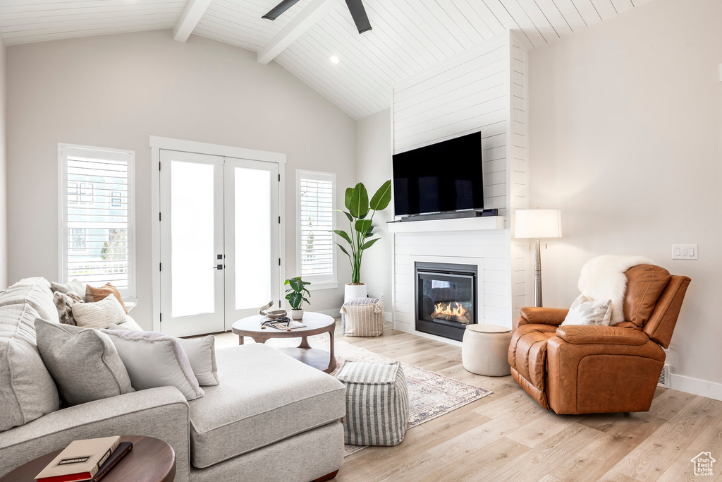 Living room with french doors, vaulted ceiling with beams, ceiling fan, a fireplace, and light hardwood / wood-style floors