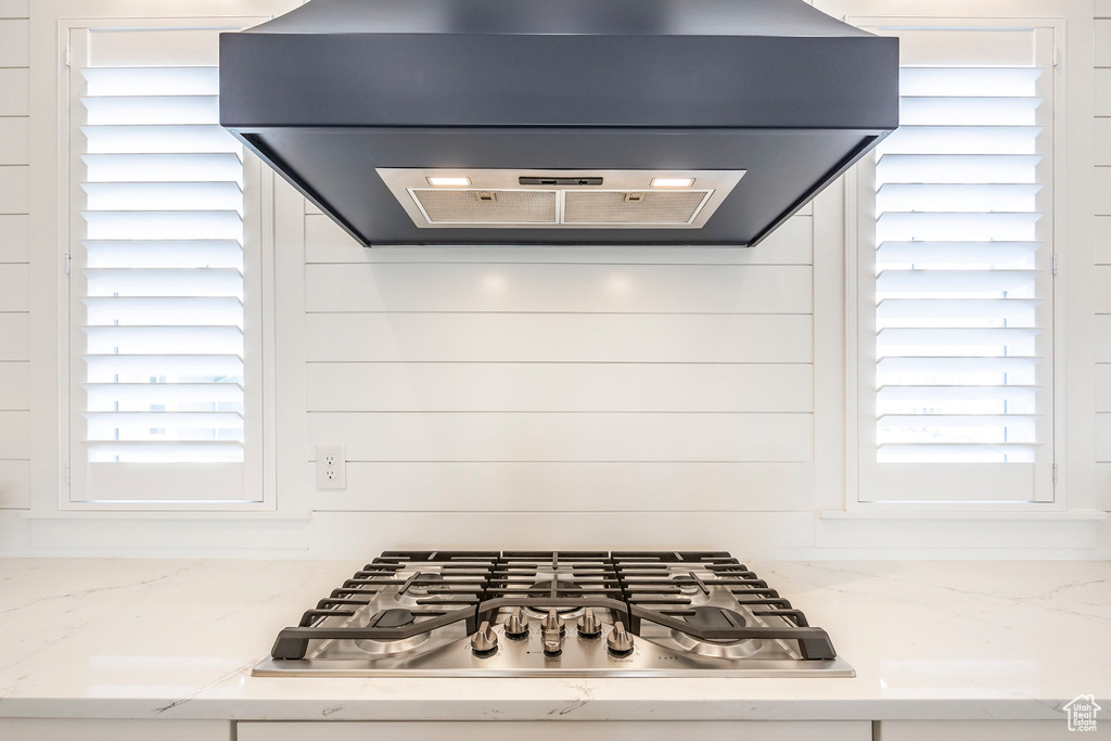 Kitchen featuring ventilation hood, light stone countertops, stainless steel gas cooktop, and a wealth of natural light