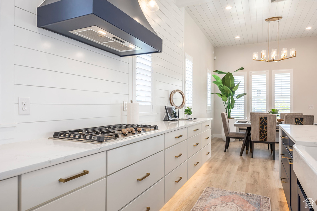 Kitchen with pendant lighting, stainless steel gas cooktop, exhaust hood, and white cabinets