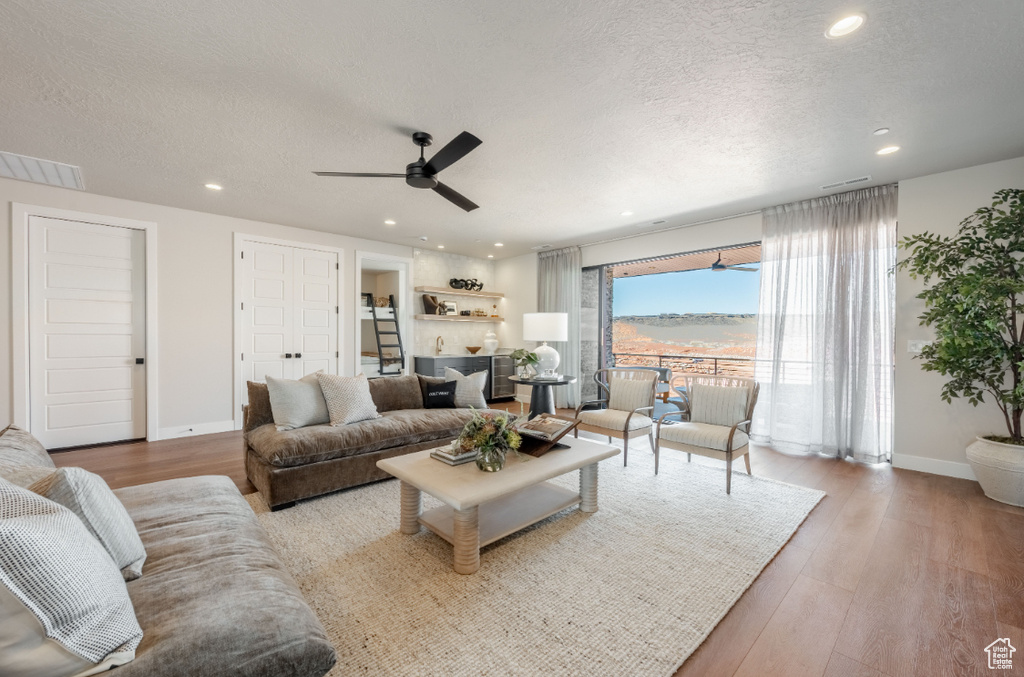 Living area featuring a textured ceiling, ceiling fan, recessed lighting, baseboards, and wood finished floors