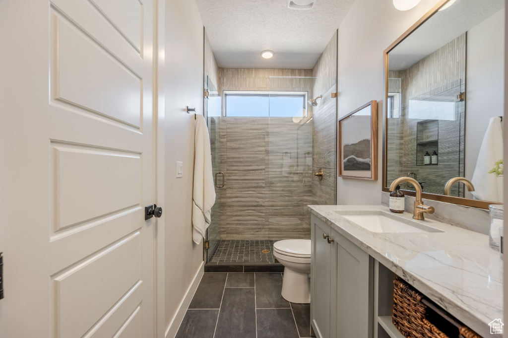 Bathroom featuring tile patterned flooring, a stall shower, toilet, vanity, and a textured ceiling