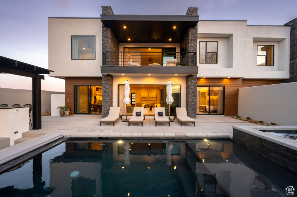 Rear view of house featuring a balcony, stone siding, a patio area, and an in-ground hot tub