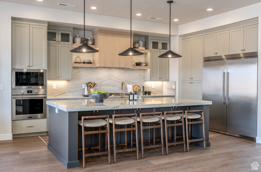 Kitchen with built in appliances, a kitchen island with sink, a breakfast bar, light wood-type flooring, and recessed lighting