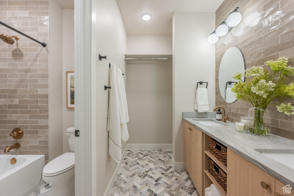 Bathroom featuring toilet, double vanity, baseboards, and shower / bathtub combination