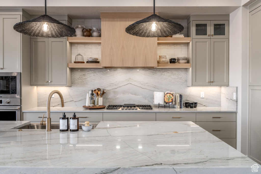 Kitchen featuring open shelves, appliances with stainless steel finishes, light stone countertops, and decorative backsplash