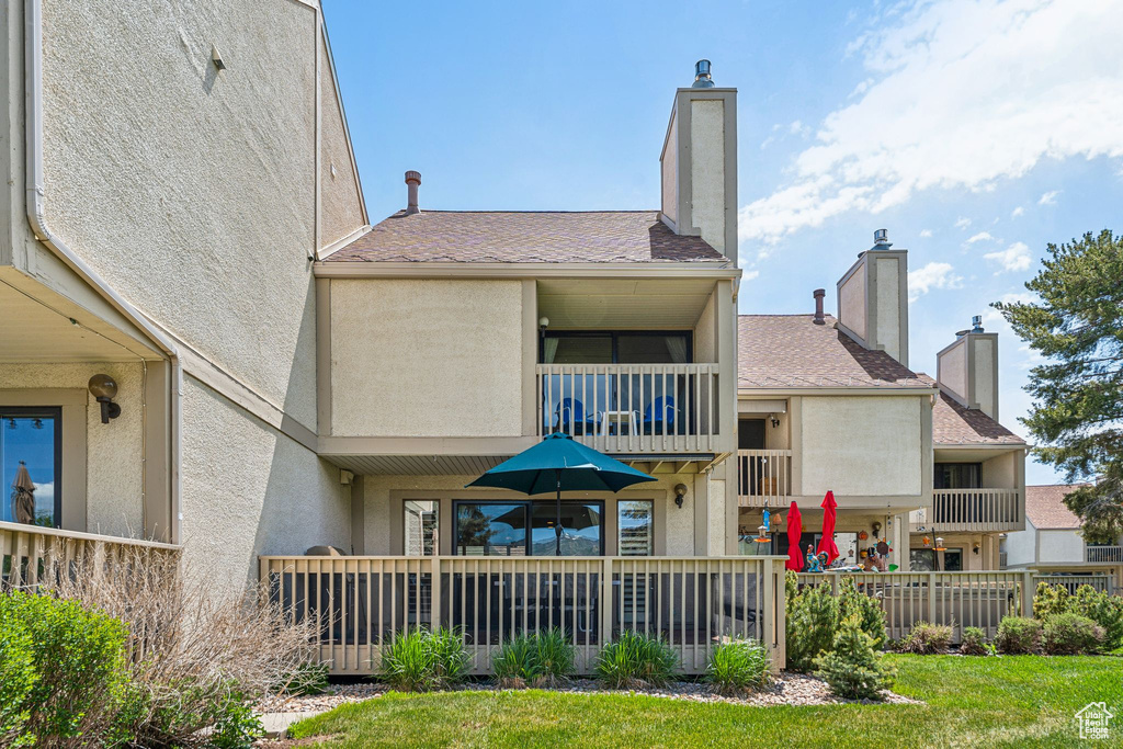 Back of house with a balcony, stucco siding, and a chimney