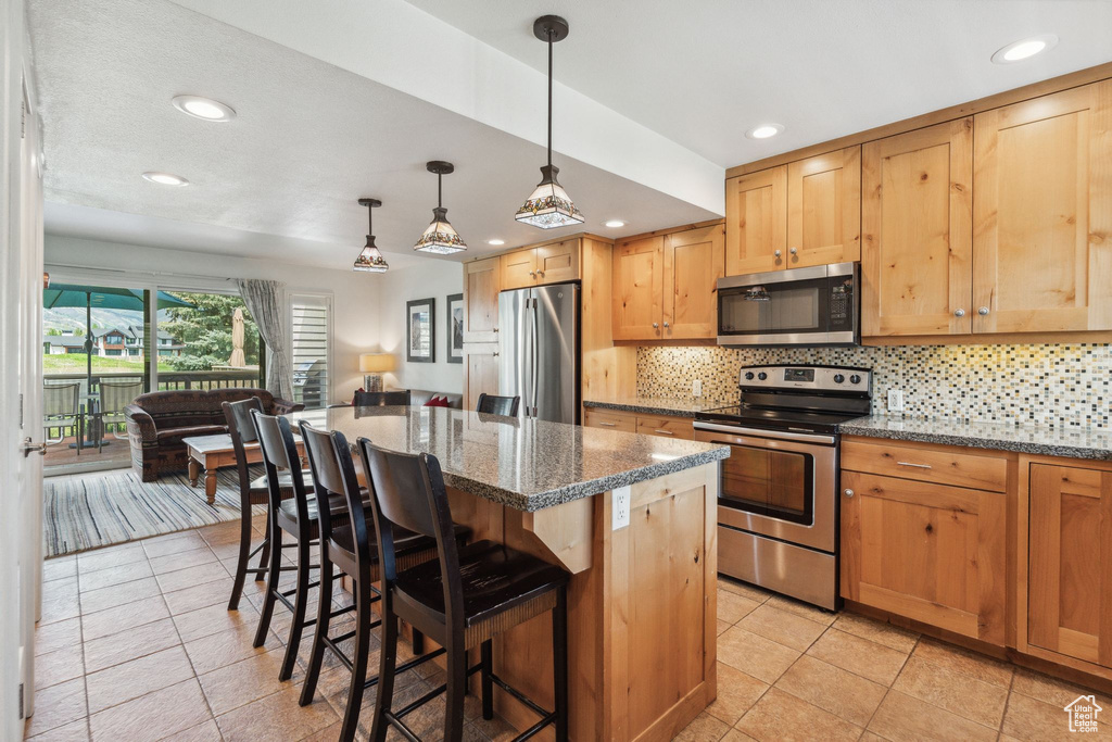 Kitchen with appliances with stainless steel finishes, a kitchen bar, backsplash, light tile patterned flooring, and recessed lighting