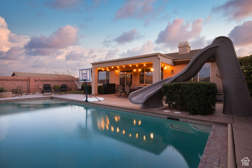 Pool at dusk featuring a patio area, a fenced in pool, fence, and a water slide