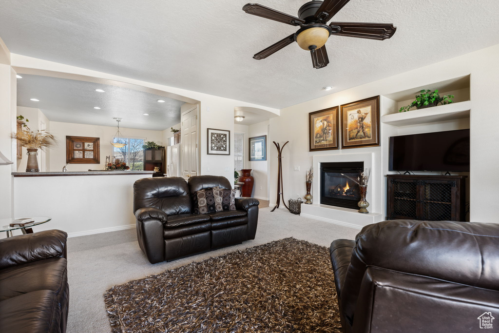 Carpeted living room with ceiling fan, built in features, and a textured ceiling