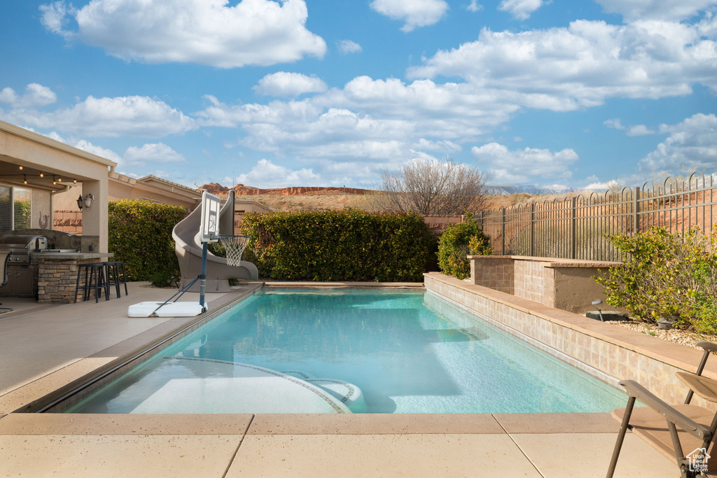 View of pool with outdoor dry bar, area for grilling, a patio area, a water slide, and a fenced backyard
