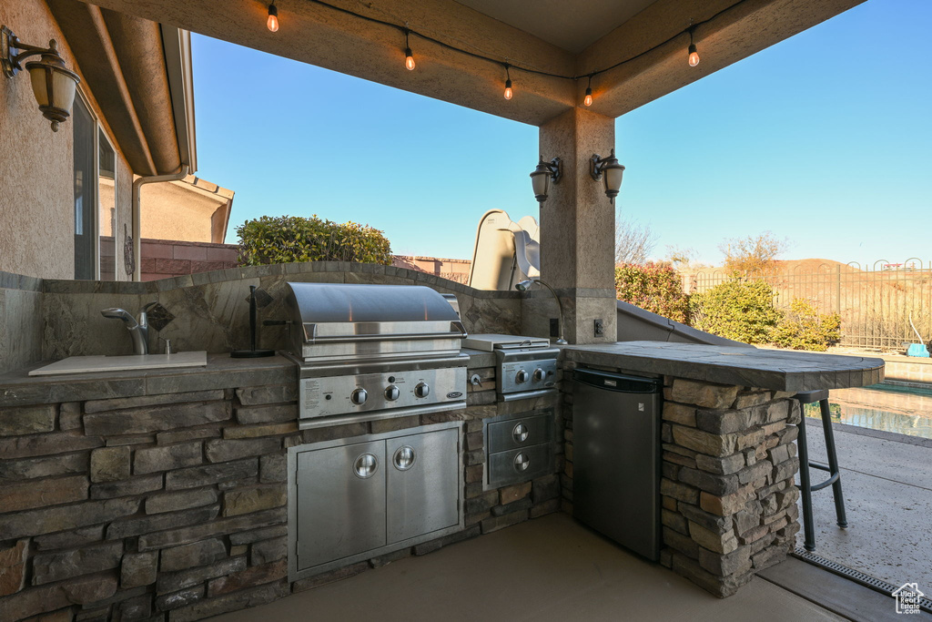 View of patio with exterior kitchen, a grill, and sink
