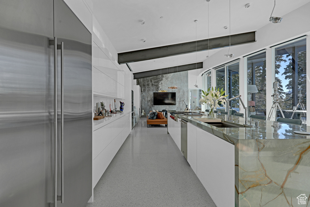 Kitchen featuring sink, stainless steel appliances, white cabinets, stone countertops, and decorative light fixtures