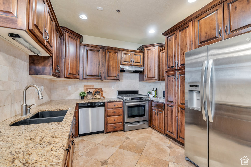 Kitchen featuring light stone counters, appliances with stainless steel finishes, sink, and decorative backsplash