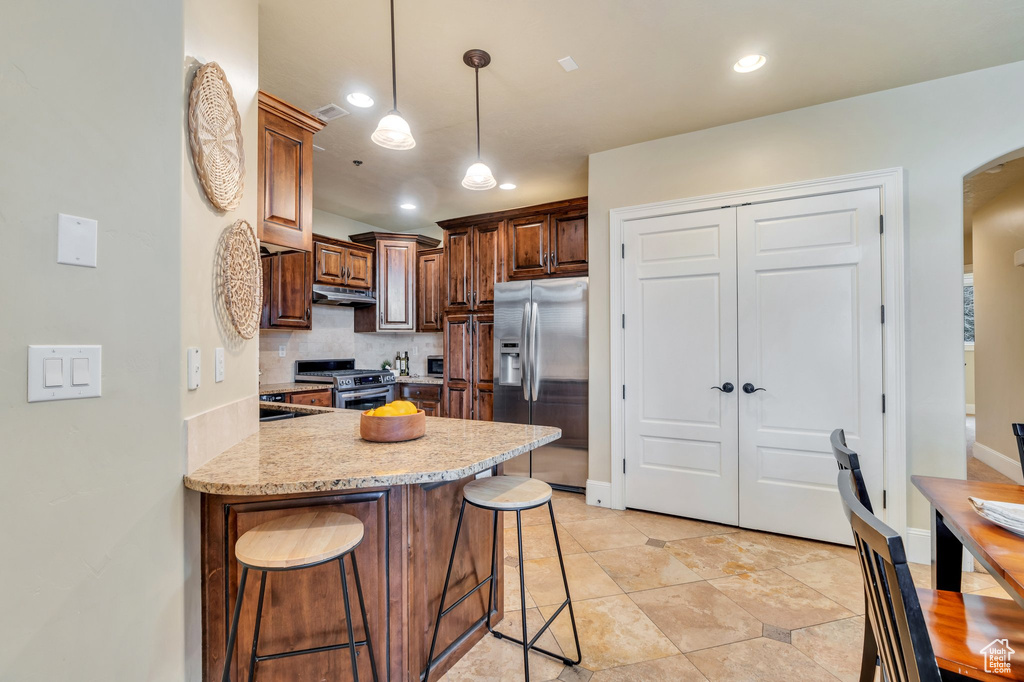 Kitchen featuring light stone counters, decorative light fixtures, appliances with stainless steel finishes, a kitchen breakfast bar, and decorative backsplash