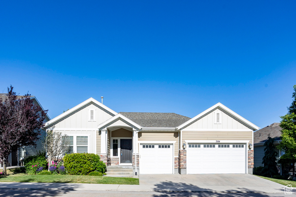 View of front facade featuring board and batten siding, a garage, concrete driveway, and stone siding