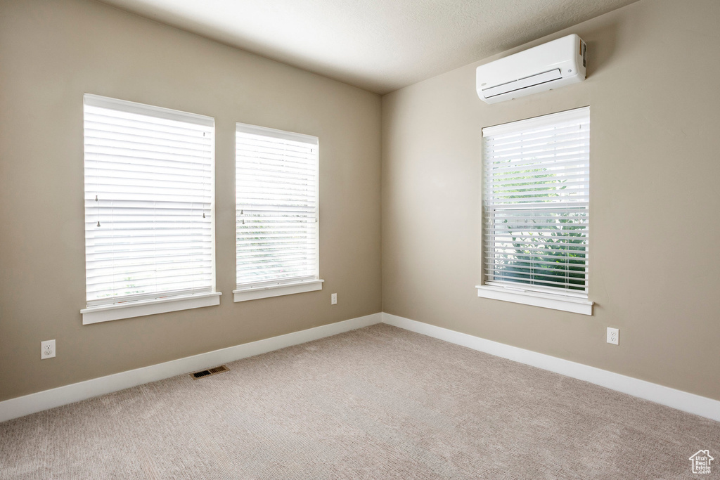 Carpeted empty room featuring a wall unit AC and baseboards