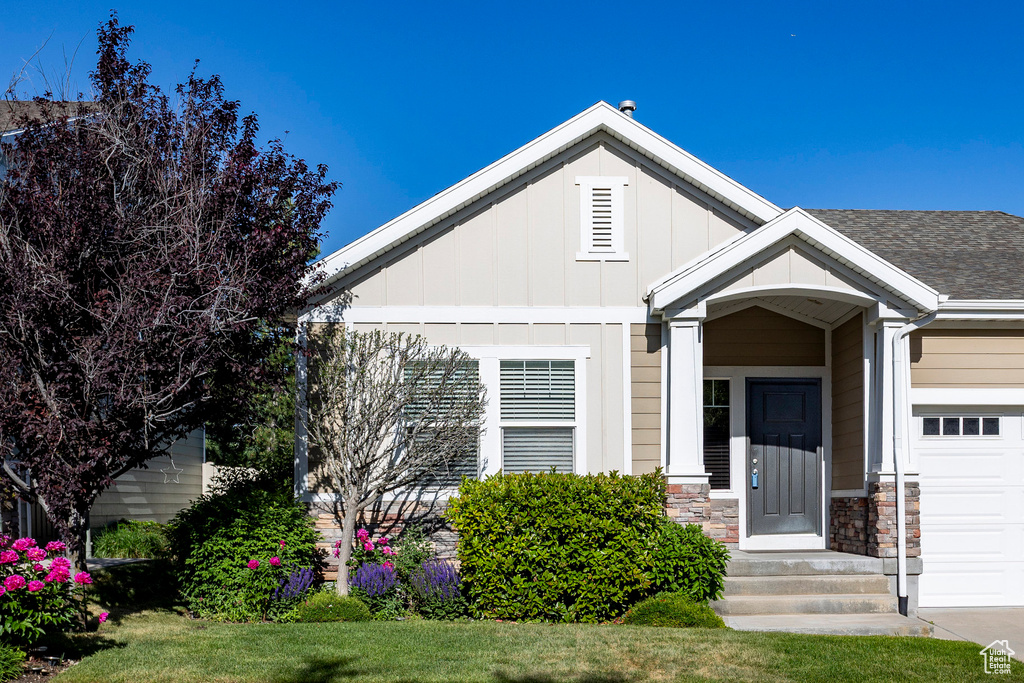 View of front of house with board and batten siding, an attached garage, stone siding, and a shingled roof
