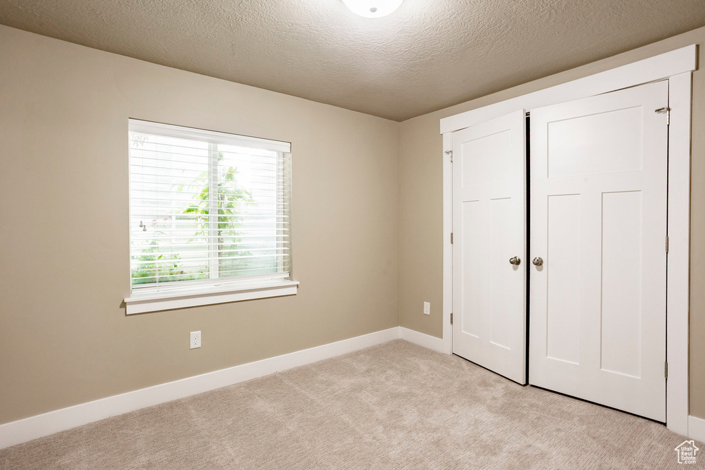 Unfurnished bedroom featuring light colored carpet, a textured ceiling, and baseboards