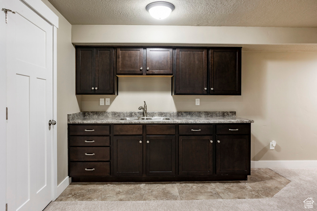 Kitchen featuring a sink, baseboards, a textured ceiling, and dark brown cabinetry