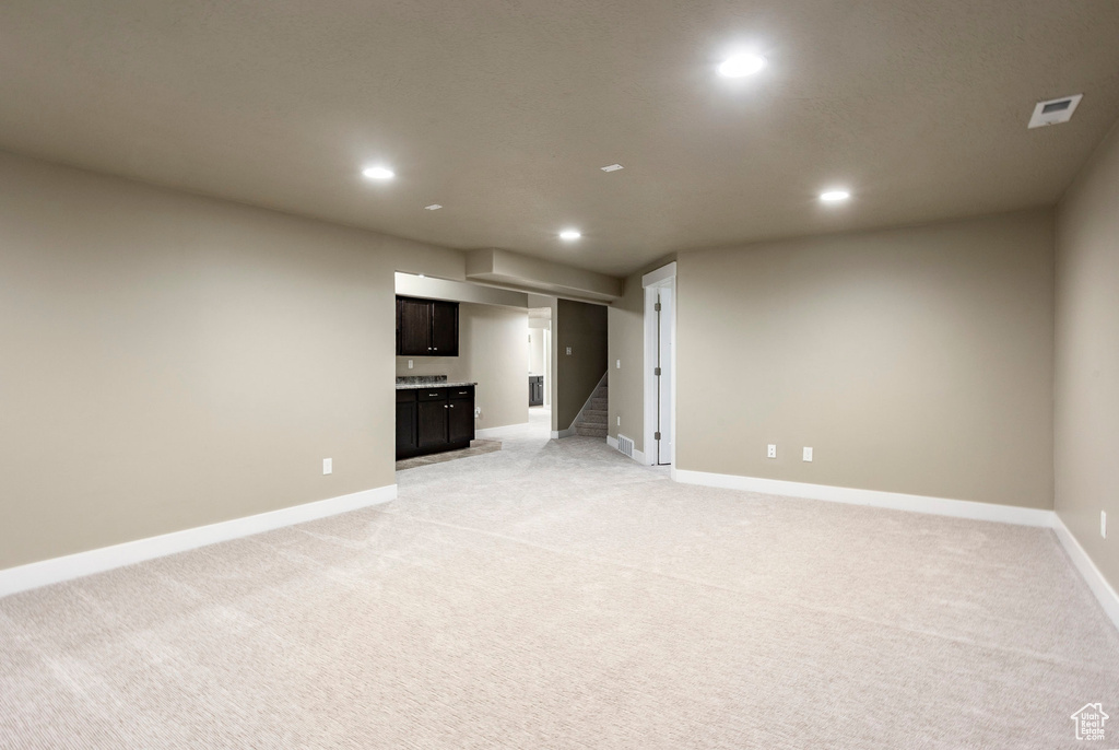 Unfurnished living room with recessed lighting, baseboards, light carpet, stairs, and bar