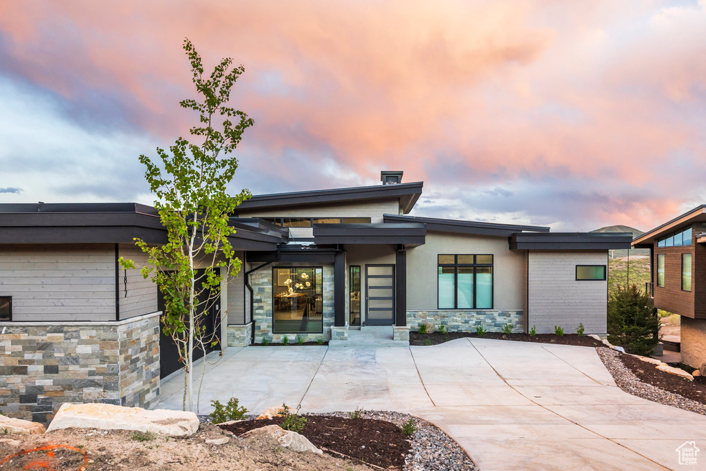 Back of property at dusk featuring stone siding and a patio