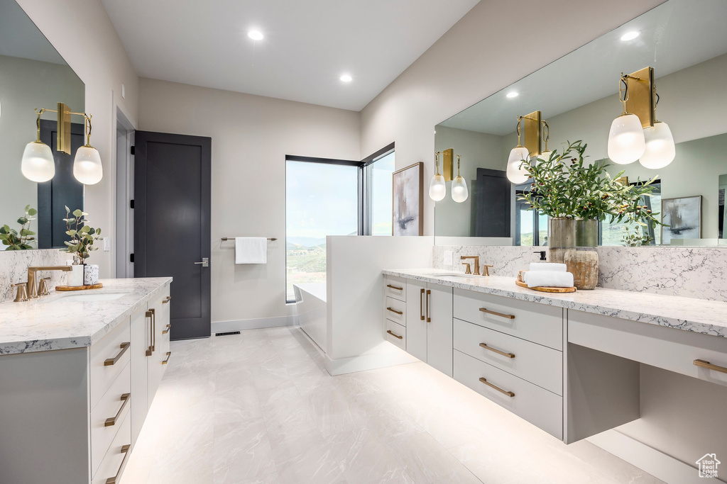 Full bath with two vanities, a garden tub, recessed lighting, and baseboards
