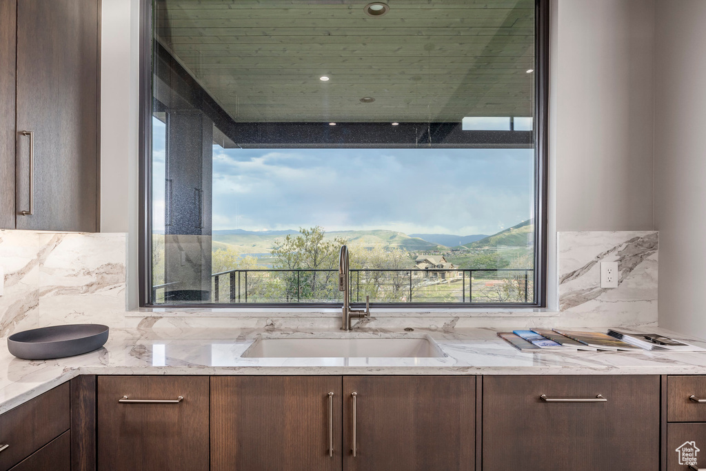 Kitchen with a sink, dark brown cabinetry, backsplash, and light stone counters