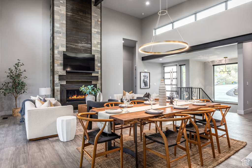 Dining room with wood finished floors, a chandelier, a large fireplace, baseboards, and a towering ceiling