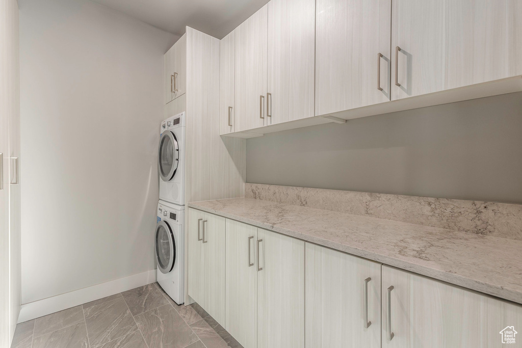 Laundry area with stacked washing machine and dryer, cabinet space, baseboards, and light marble finish flooring