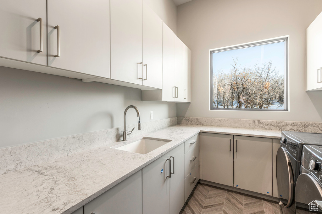 Kitchen featuring a sink, washing machine and clothes dryer, light stone counters, and white cabinets
