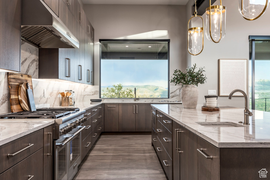 Kitchen featuring under cabinet range hood, a sink, high end range, and dark brown cabinetry