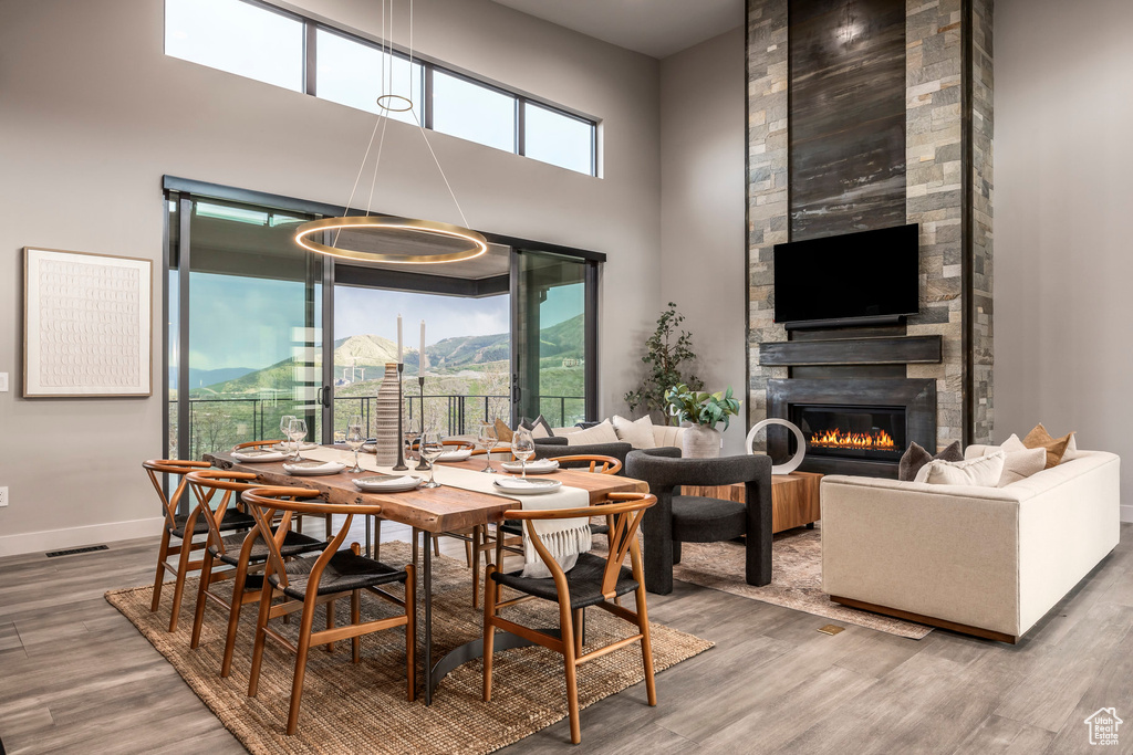 Dining space with wood finished floors, a large fireplace, a towering ceiling, and baseboards