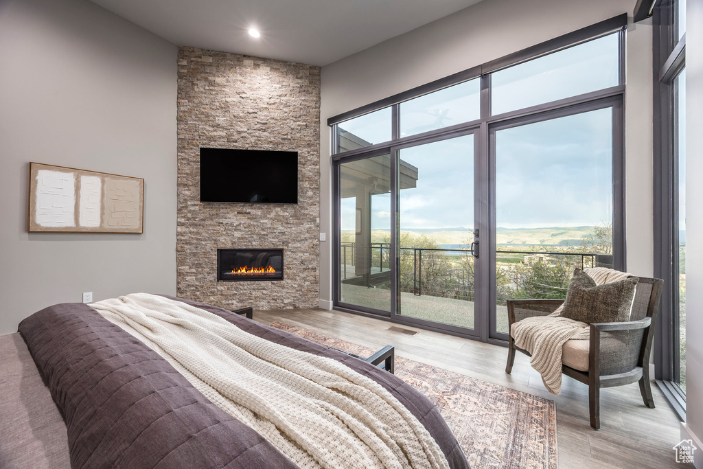 Bedroom featuring access to exterior, light wood-type flooring, a stone fireplace, and recessed lighting