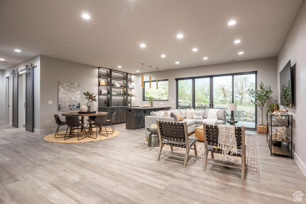 Living area with a barn door, recessed lighting, light wood finished floors, and baseboards