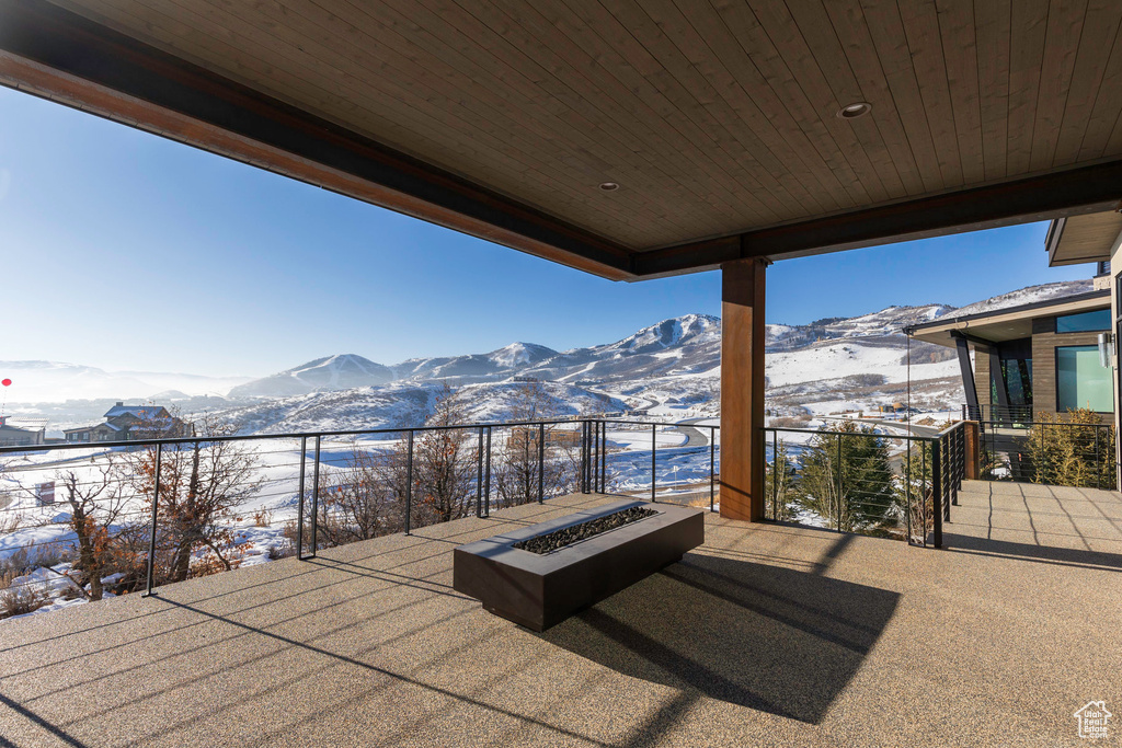 Snow covered patio featuring a mountain view, a fire pit, and a balcony