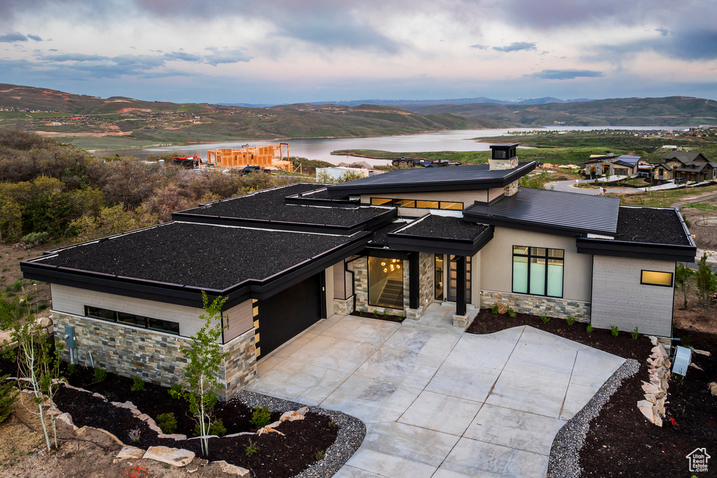 Prairie-style home featuring stone siding, driveway, a water and mountain view, and an attached garage