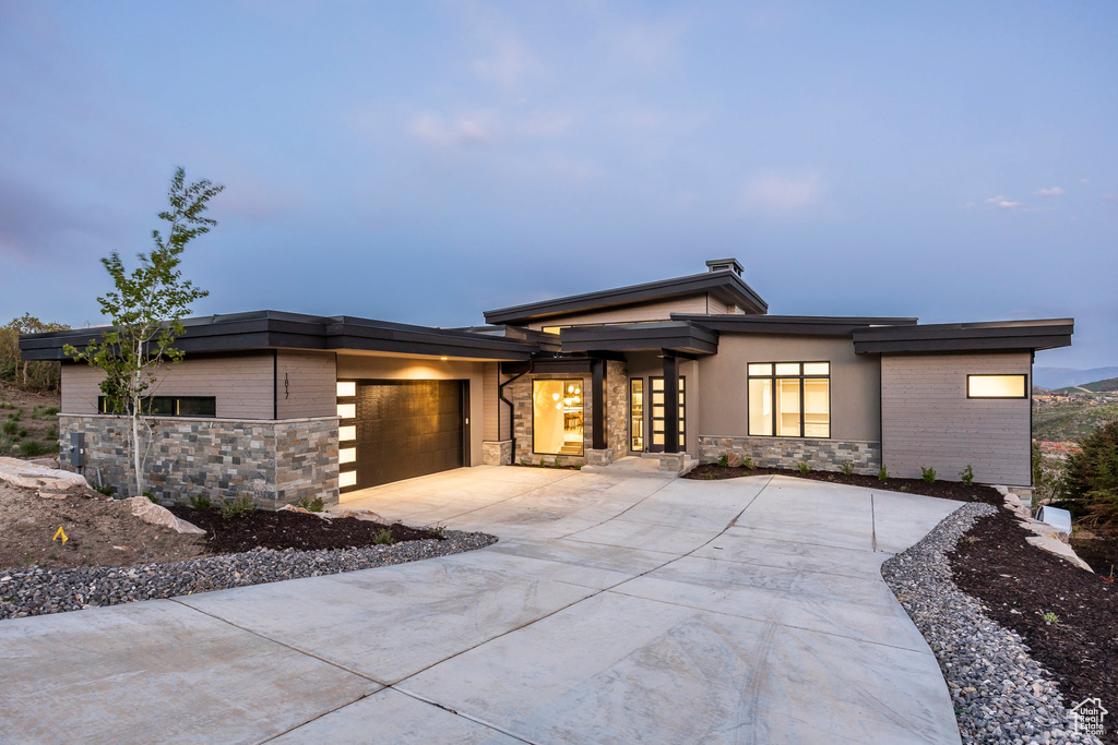 View of front of property with stone siding, concrete driveway, an attached garage, and stucco siding