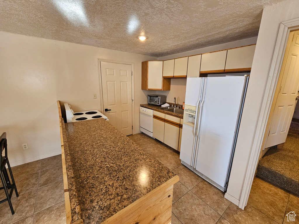 Kitchen with sink, white appliances, dark stone counters, and a textured ceiling