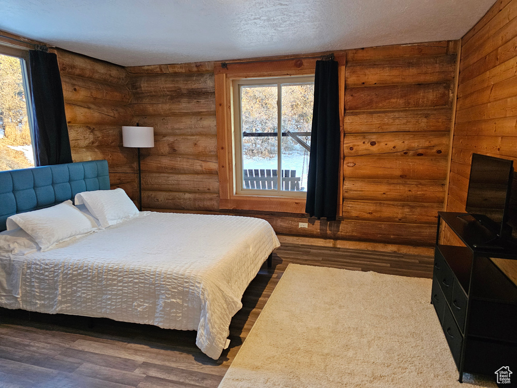 Bedroom with a textured ceiling, rustic walls, and hardwood / wood-style flooring