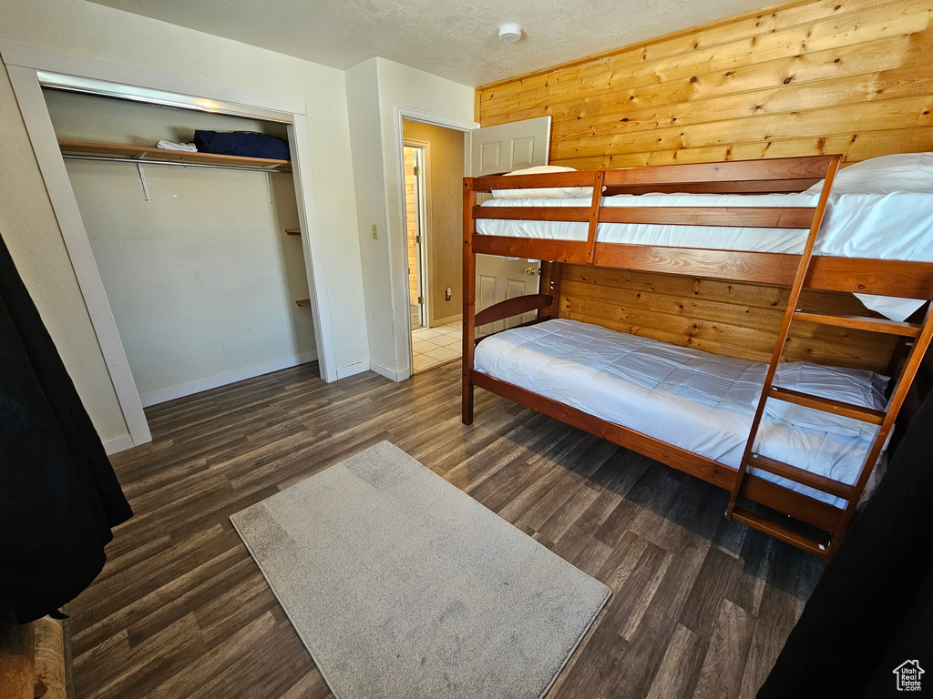 Bedroom featuring dark wood-type flooring, wood walls, and a closet