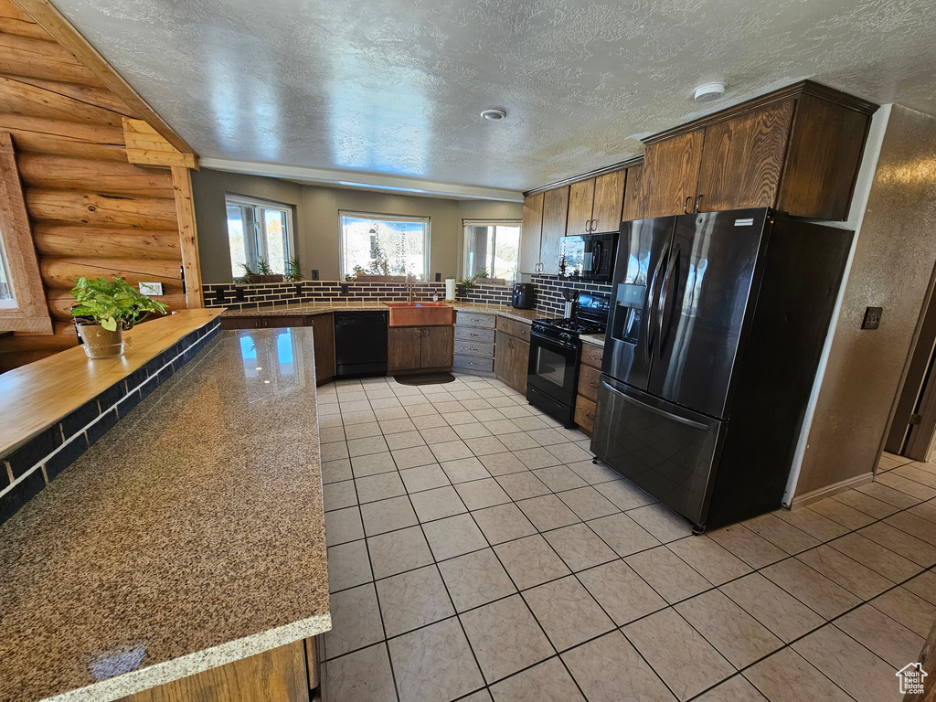 Kitchen with sink, light stone counters, kitchen peninsula, log walls, and black appliances