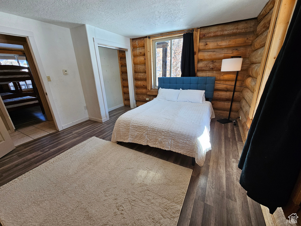 Bedroom featuring dark hardwood / wood-style flooring, rustic walls, and a textured ceiling