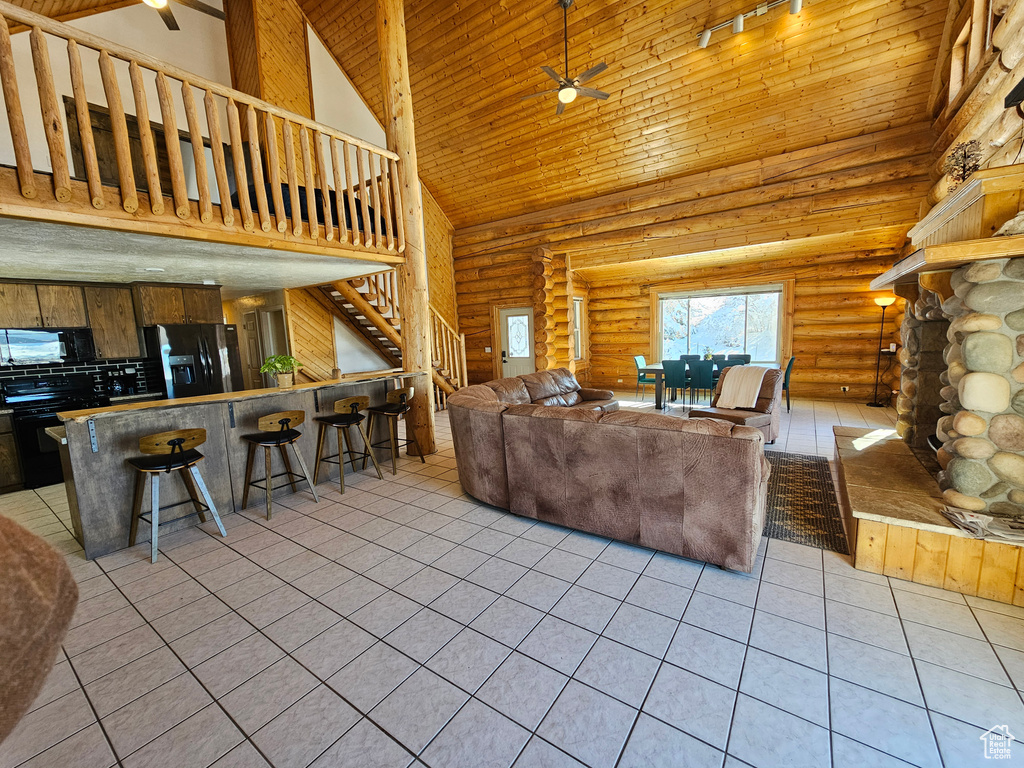 Tiled living room featuring ceiling fan, a fireplace, log walls, and high vaulted ceiling