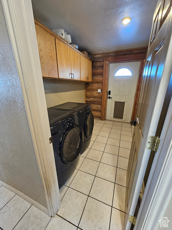 Clothes washing area with light tile patterned floors, rustic walls, cabinets, washer and dryer, and a textured ceiling