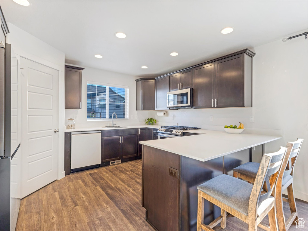 Kitchen with sink, dark wood-type flooring, appliances with stainless steel finishes, a kitchen breakfast bar, and kitchen peninsula