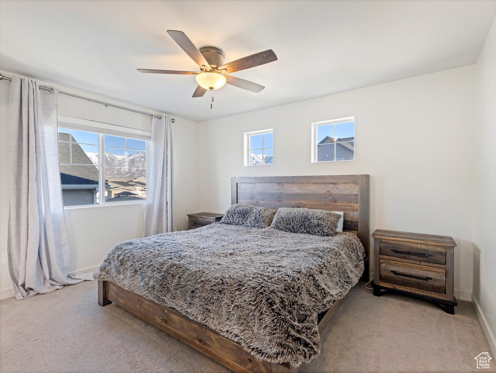 Bedroom featuring light carpet, multiple windows, and ceiling fan