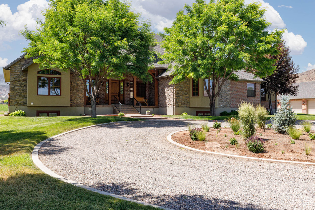 View of front facade featuring curved driveway, a front lawn, stone siding, covered porch, and brick siding